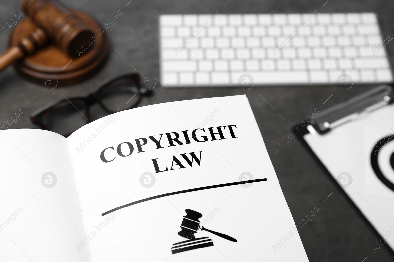 Photo of Book with words COPYRIGHT LAW, computer keyboard and gavel on table, closeup