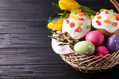 Photo of Traditional Easter cakes and eggs in wicker basket on dark table. Space for text