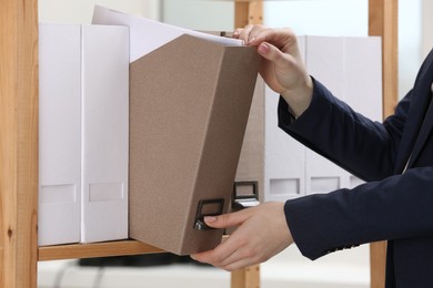 Photo of Woman taking folder with documents from shelf in office, closeup