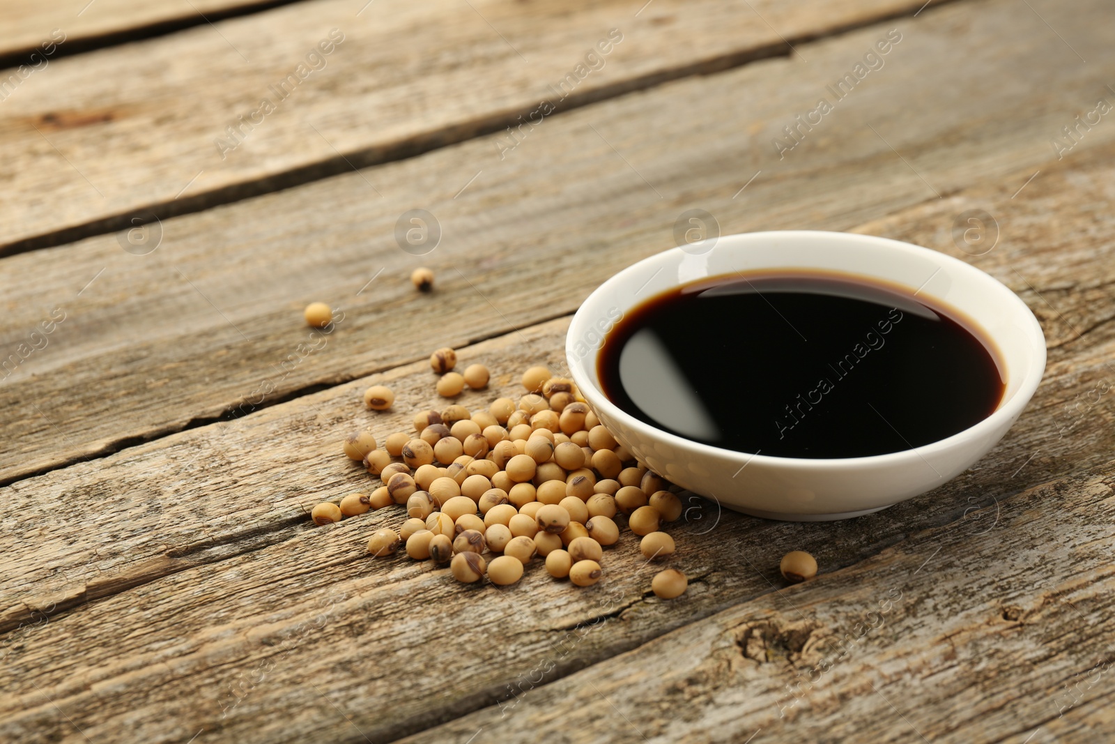 Photo of Soy sauce in bowl and beans on wooden table. Space for text