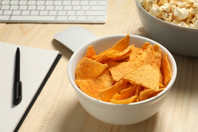 Photo of Bad eating habits at workplace. Tasty tortilla chips in bowl on wooden table, closeup