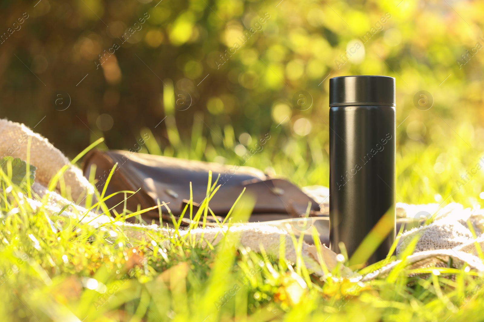 Photo of Black thermos and blanket on green grass outdoors