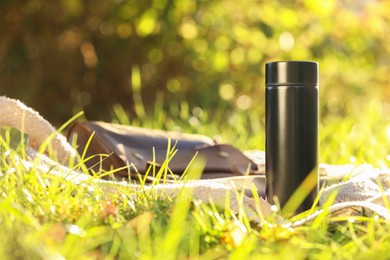 Photo of Black thermos and blanket on green grass outdoors