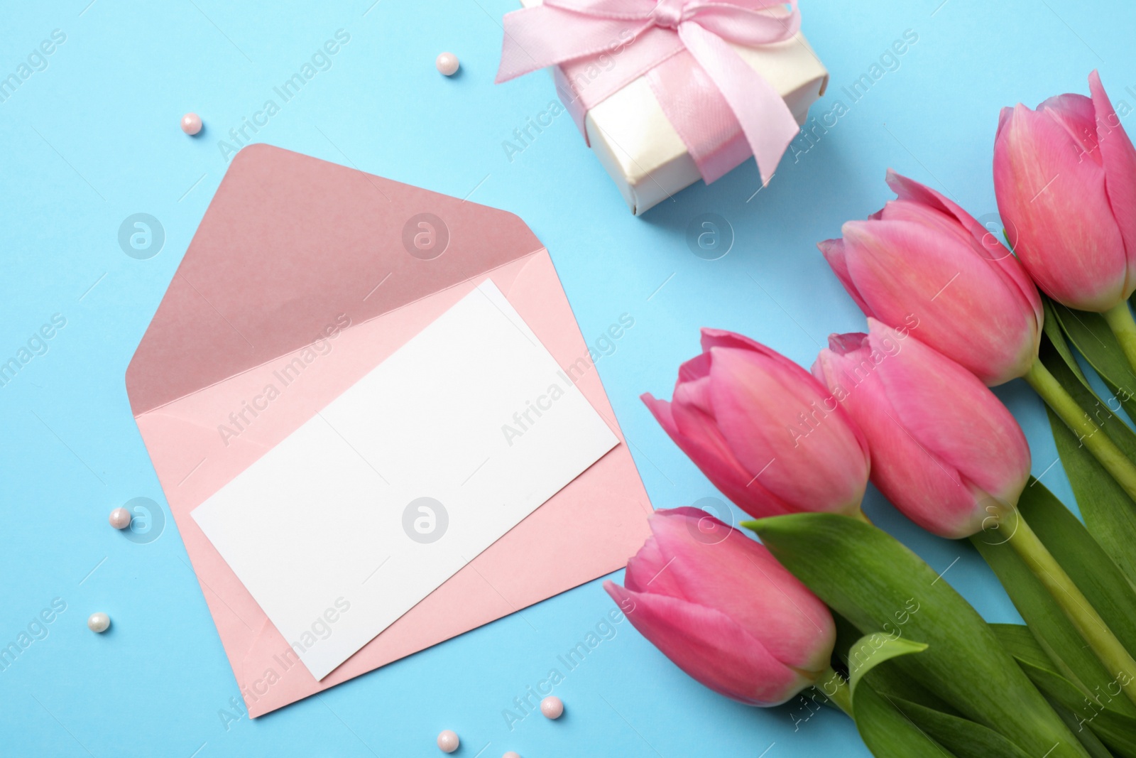 Photo of Flat lay composition with tulips and card on light blue background, space for text. Happy Mother's day