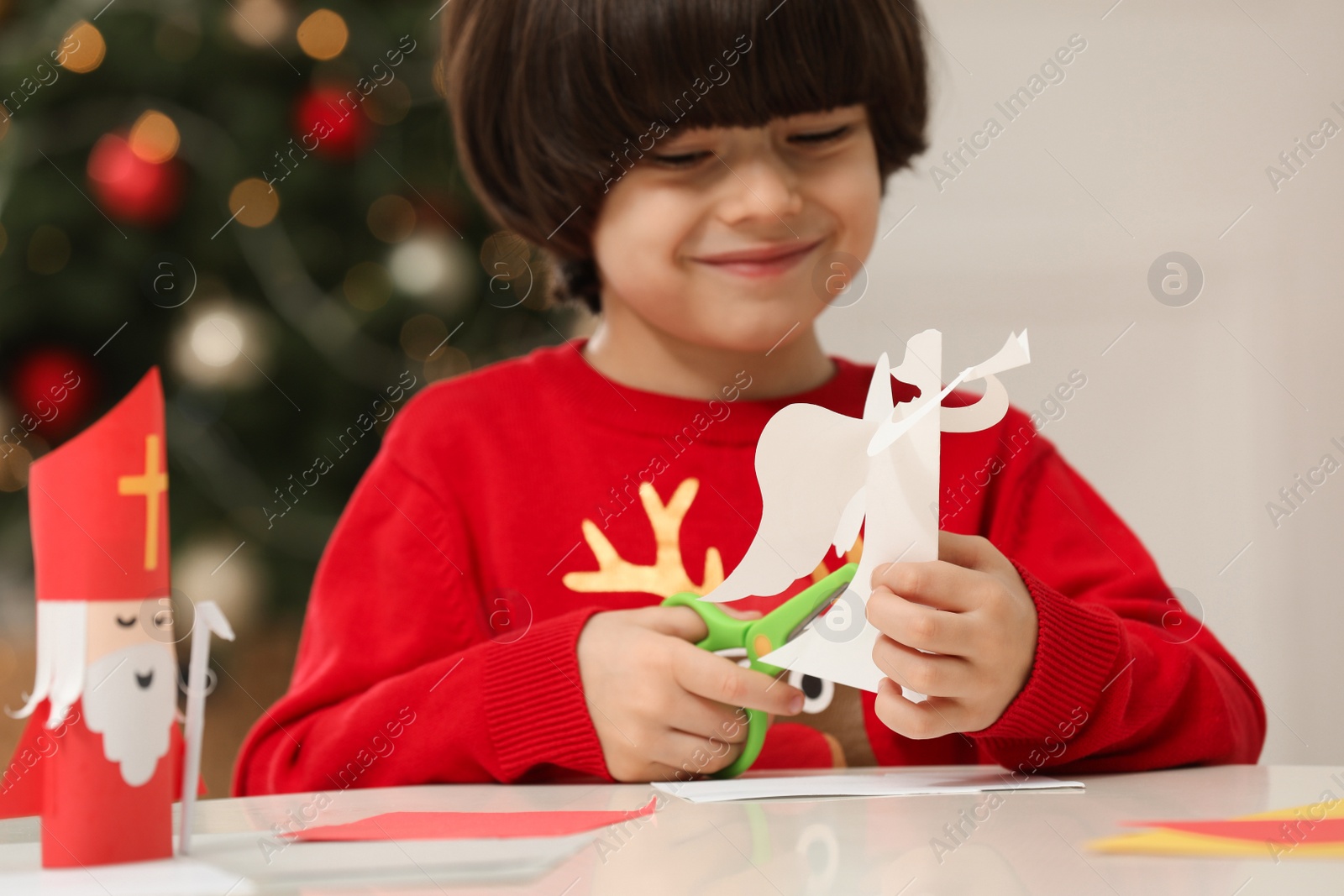 Photo of Cute little boy making paper angel for Saint Nicholas day at home, focus on hands