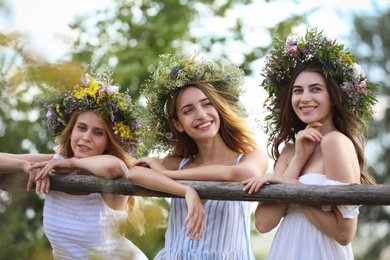 Photo of Young women wearing wreaths made of beautiful flowers near wooden fence