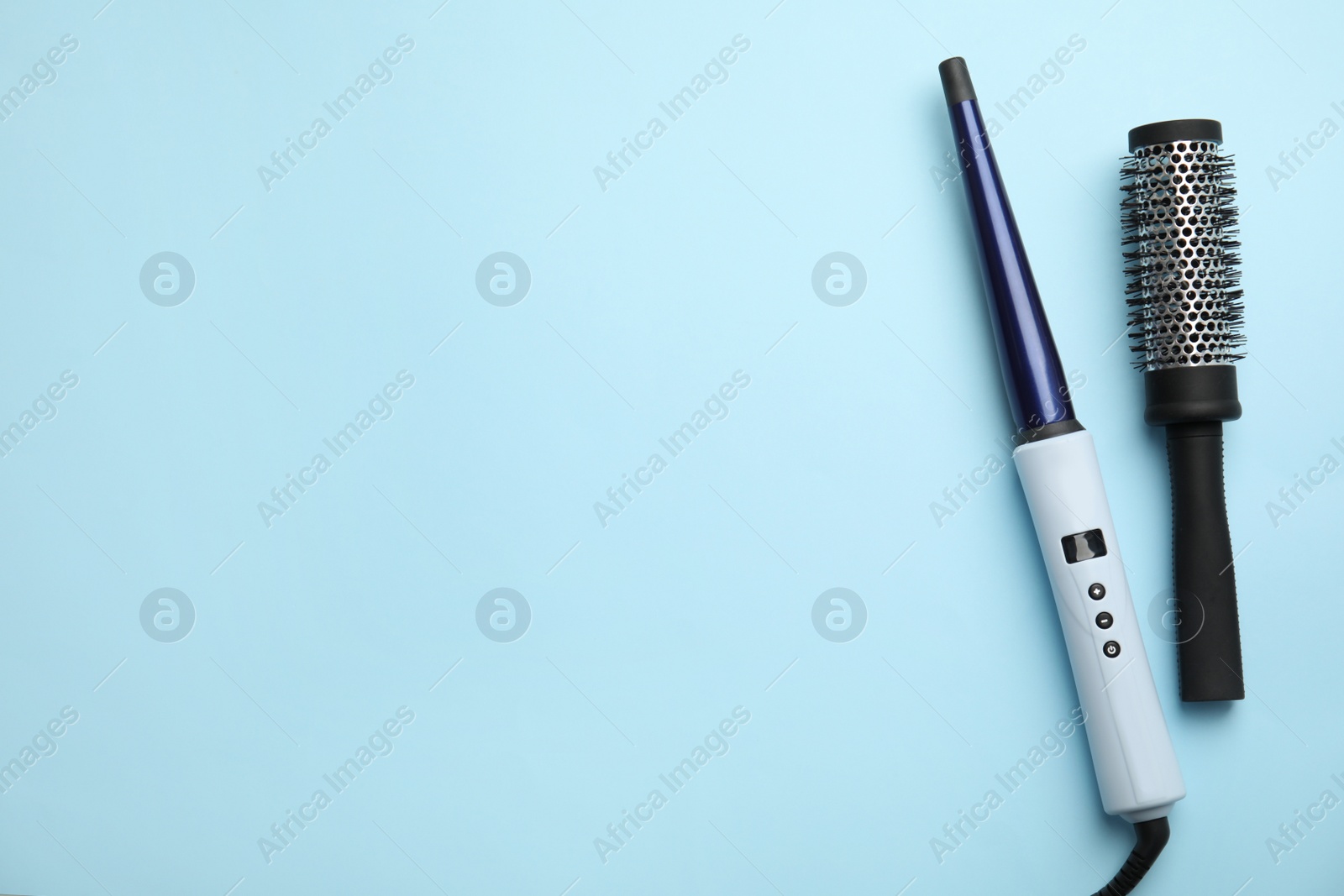 Photo of Curling iron and hair brush on light blue background, flat lay. Space for text