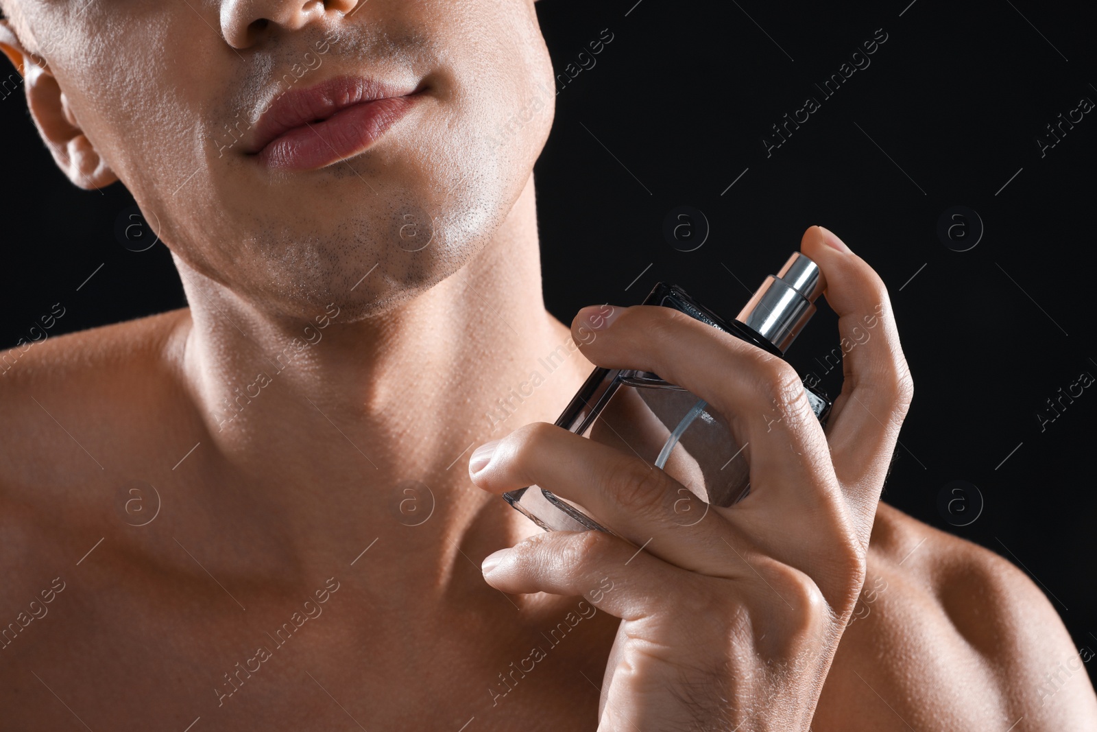 Photo of Young man using perfume on black background, closeup