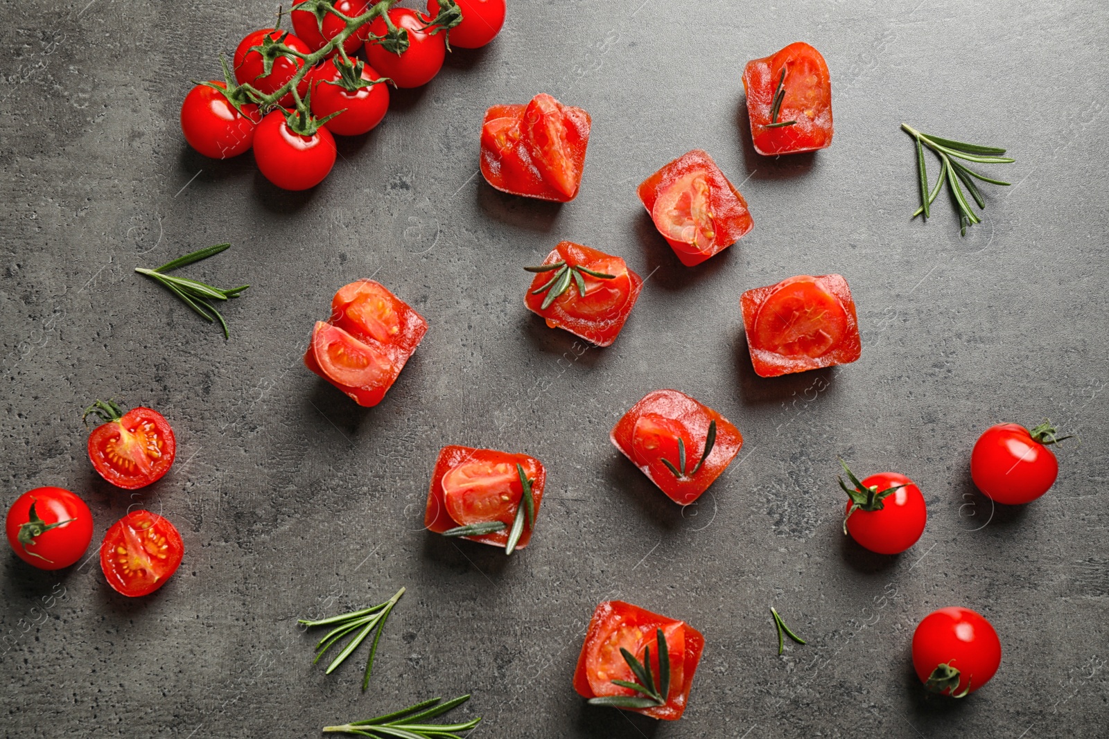 Photo of Ice cubes with tomatoes and rosemary on grey table, flat lay