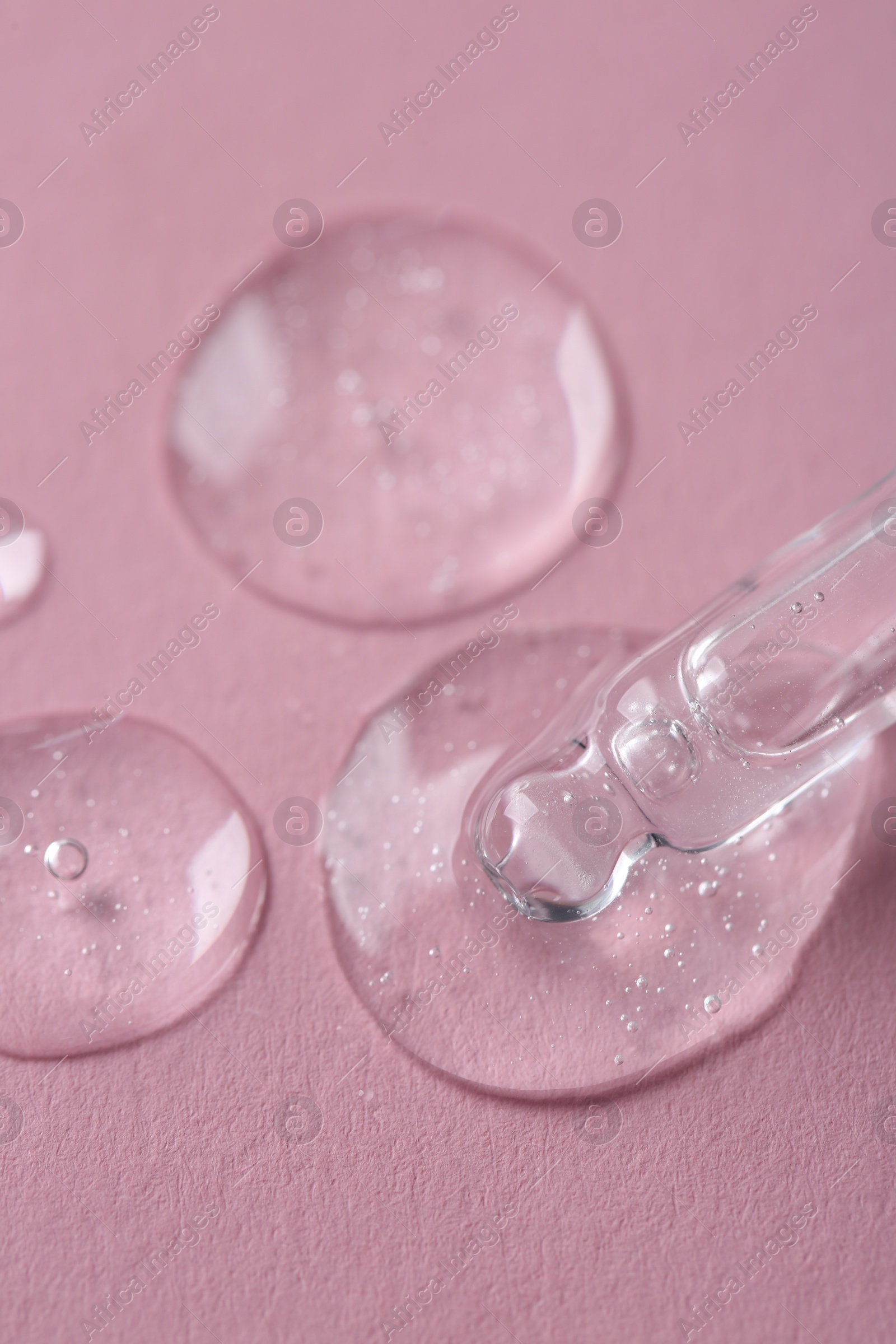 Photo of Dripping cosmetic serum from pipette onto pink background, macro view