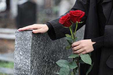Photo of Woman with red roses near grey granite tombstone outdoors, closeup. Funeral ceremony