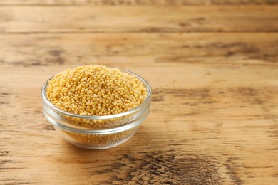 Photo of Millet groats in bowl on wooden table, space for text