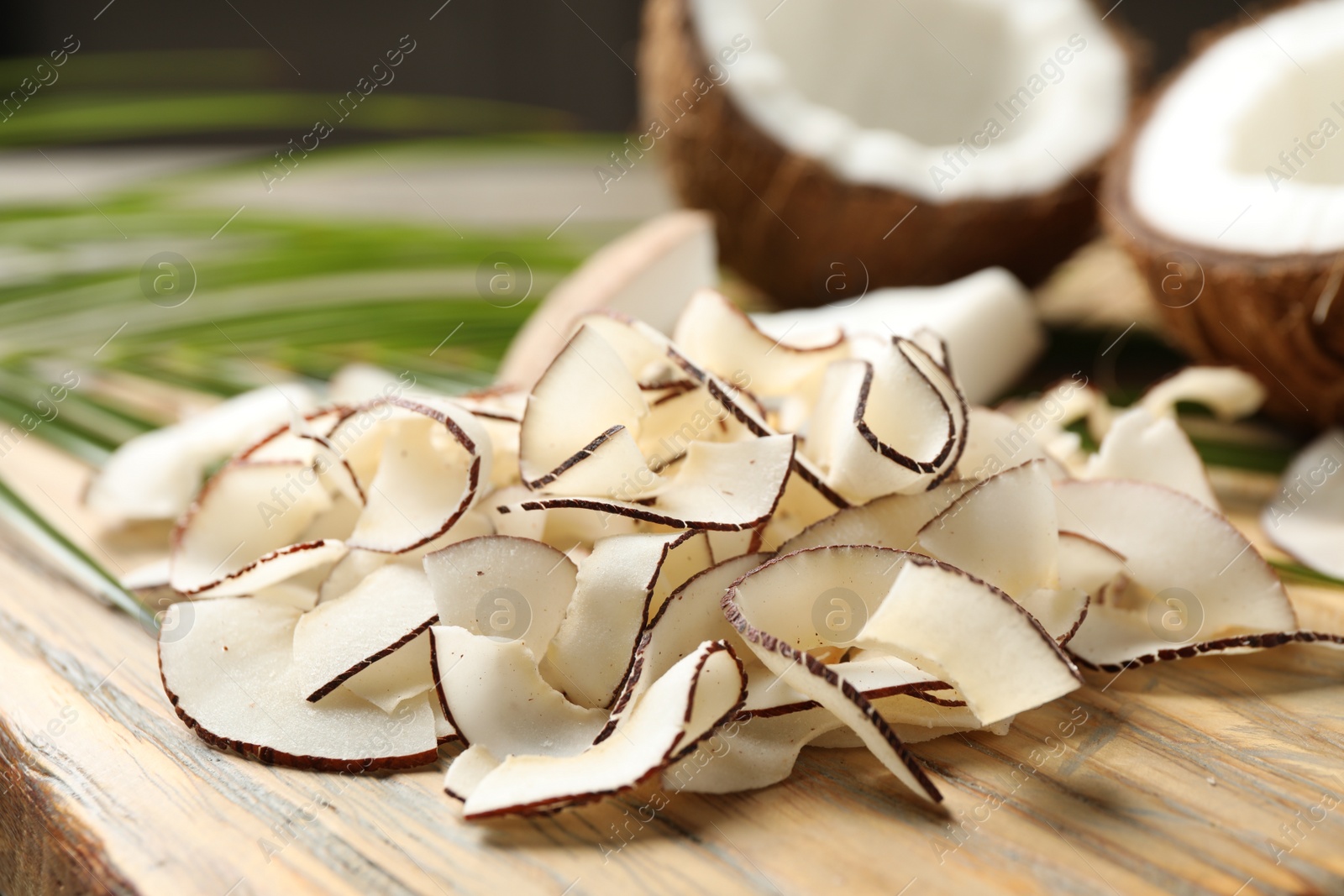 Photo of Pile of tasty coconut chips on wooden board, closeup