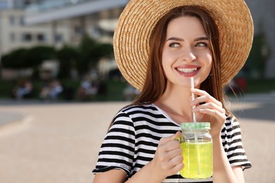 Photo of Young woman in straw hat with plastic cup of fresh juice outdoors, space for text