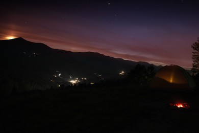 Beautiful view of mountain landscape with bonfire and camping tent in twilight