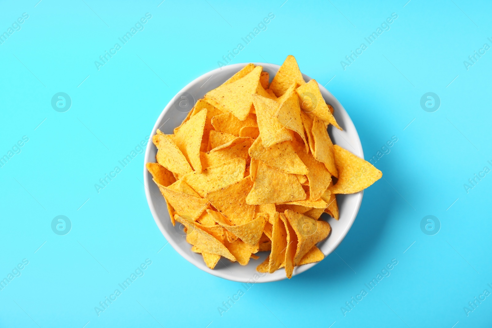 Photo of Tasty mexican nachos chips in bowl on blue background, top view