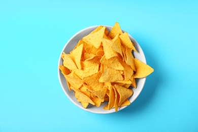 Photo of Tasty mexican nachos chips in bowl on blue background, top view