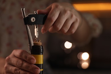 Woman opening wine bottle with corkscrew on blurred background, closeup