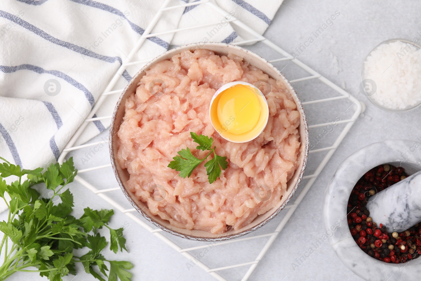 Photo of Flat lay composition with fresh raw minced meat, parsley and egg in bowl on light grey table