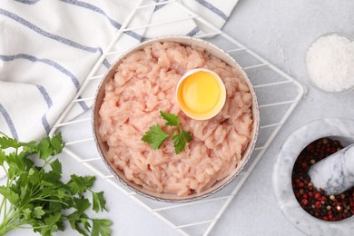 Flat lay composition with fresh raw minced meat, parsley and egg in bowl on light grey table