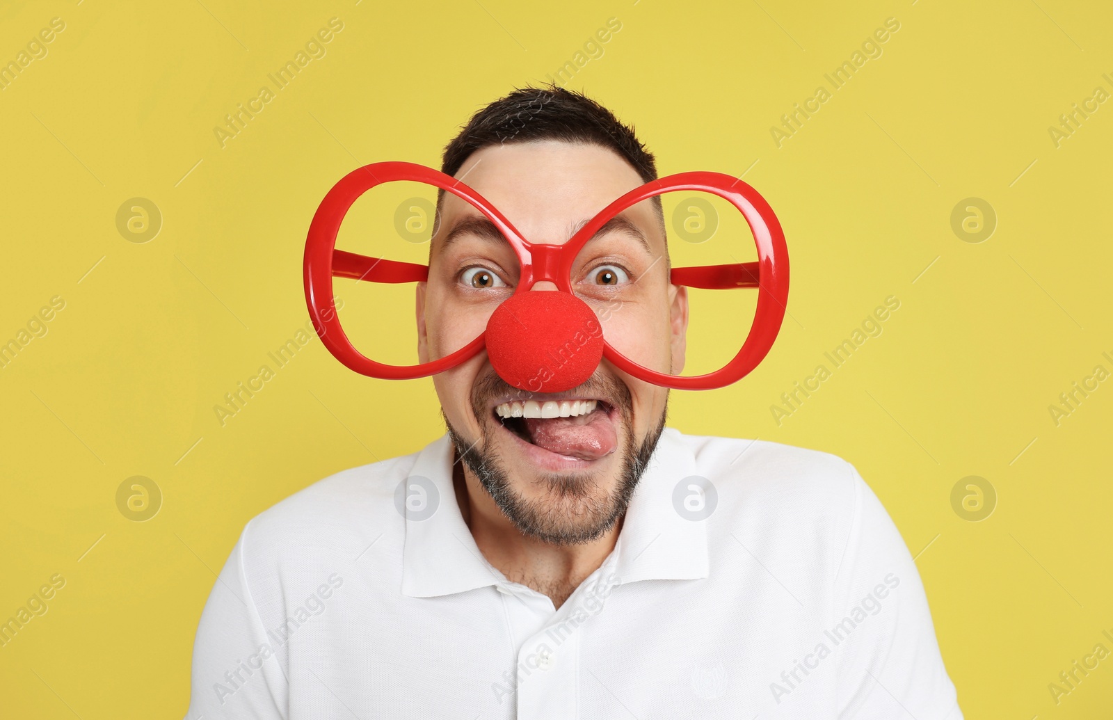 Photo of Funny man with clown nose and large glasses on yellow background. April fool's day