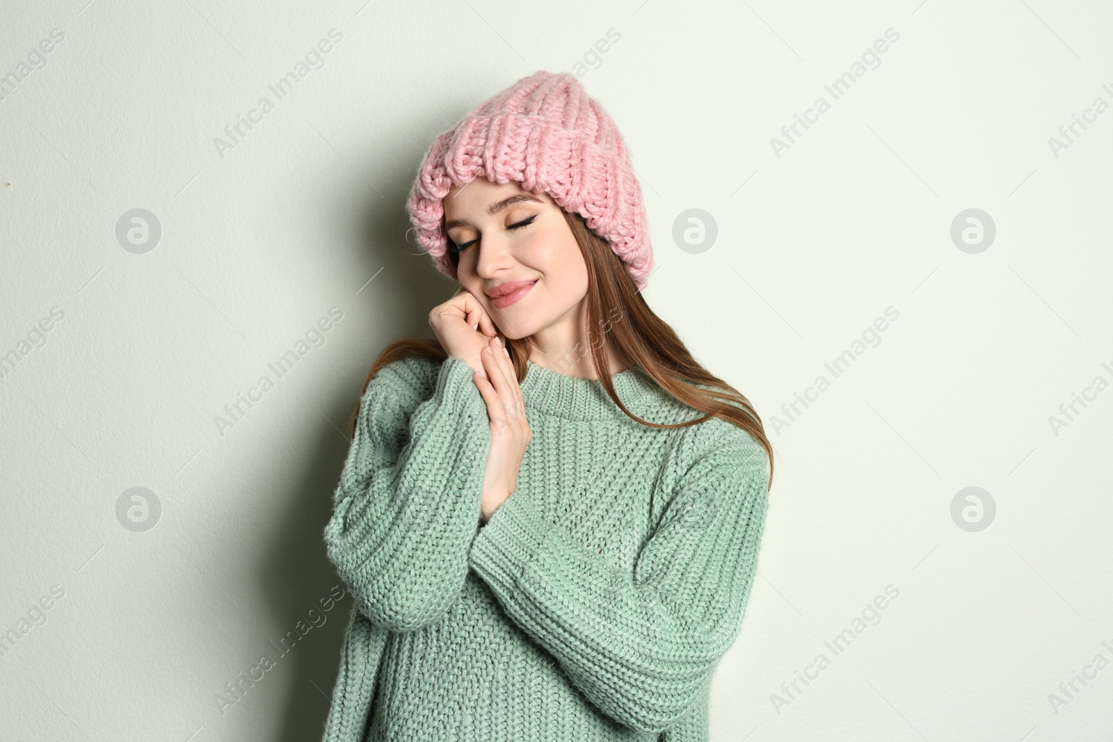 Photo of Young woman wearing warm sweater and hat on light background. Winter season
