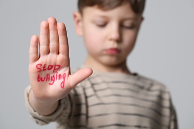 Photo of Boy showing hand with phrase Stop Bullying on light grey background, selective focus. Space for text
