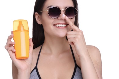 Beautiful young woman in sunglasses holding bottle of sun protection cream on white background