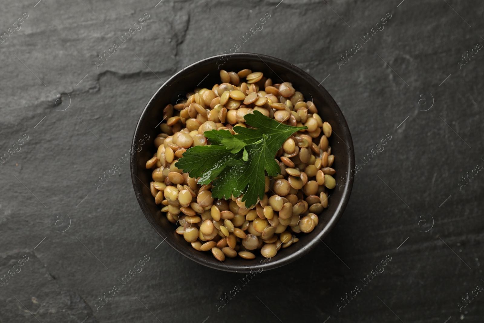 Photo of Delicious lentils with parsley in bowl on grey textured table, top view