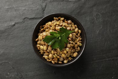 Photo of Delicious lentils with parsley in bowl on grey textured table, top view