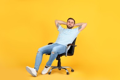 Young man relaxing in comfortable office chair on yellow background