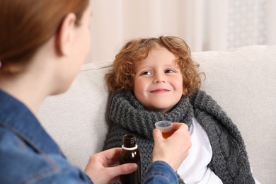 Photo of Mother giving cough syrup to her son on sofa