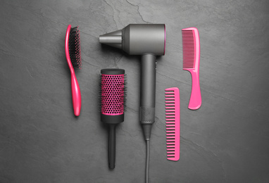 Photo of Hair dryer and different brushes on black background, flat lay. Professional hairdresser tool