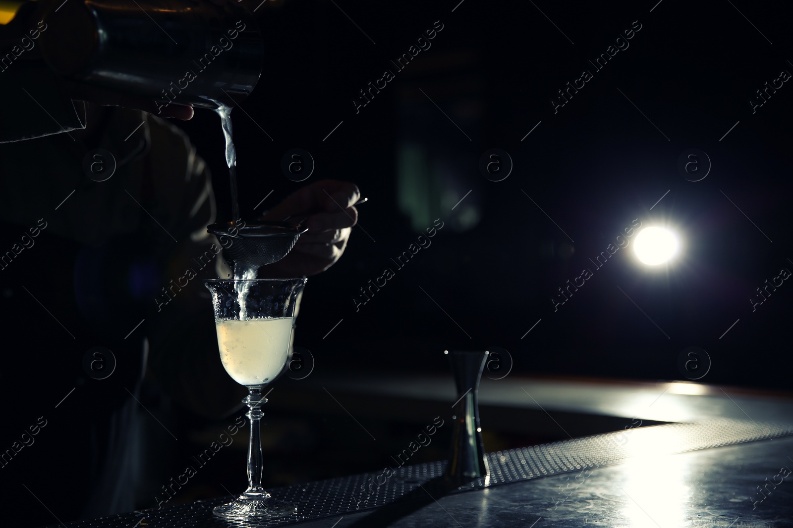 Photo of Barman pouring martini cocktail into glass at counter, closeup. Space for text