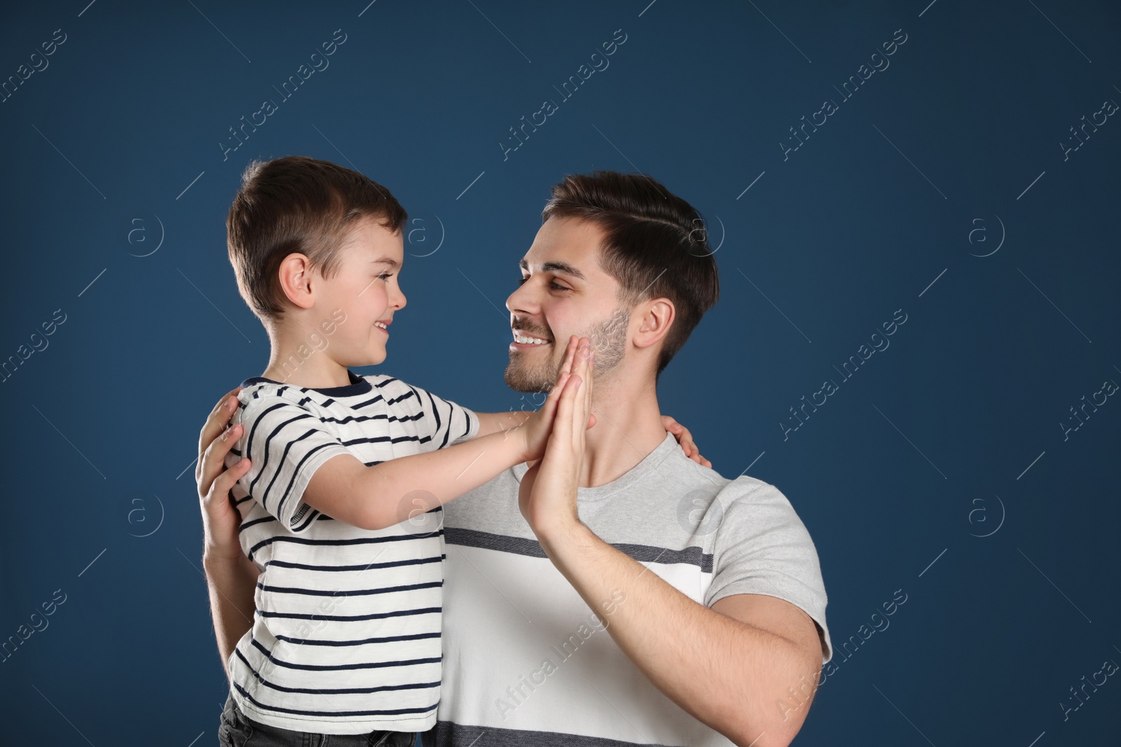 Photo of Portrait of dad and his son giving high five on color background