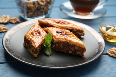 Photo of Delicious sweet baklava with walnuts and mint on blue wooden table, closeup