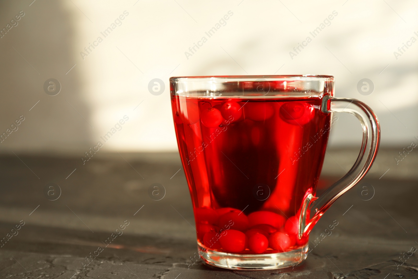 Photo of Tasty hot cranberry tea with fresh berries in glass cup on black textured table