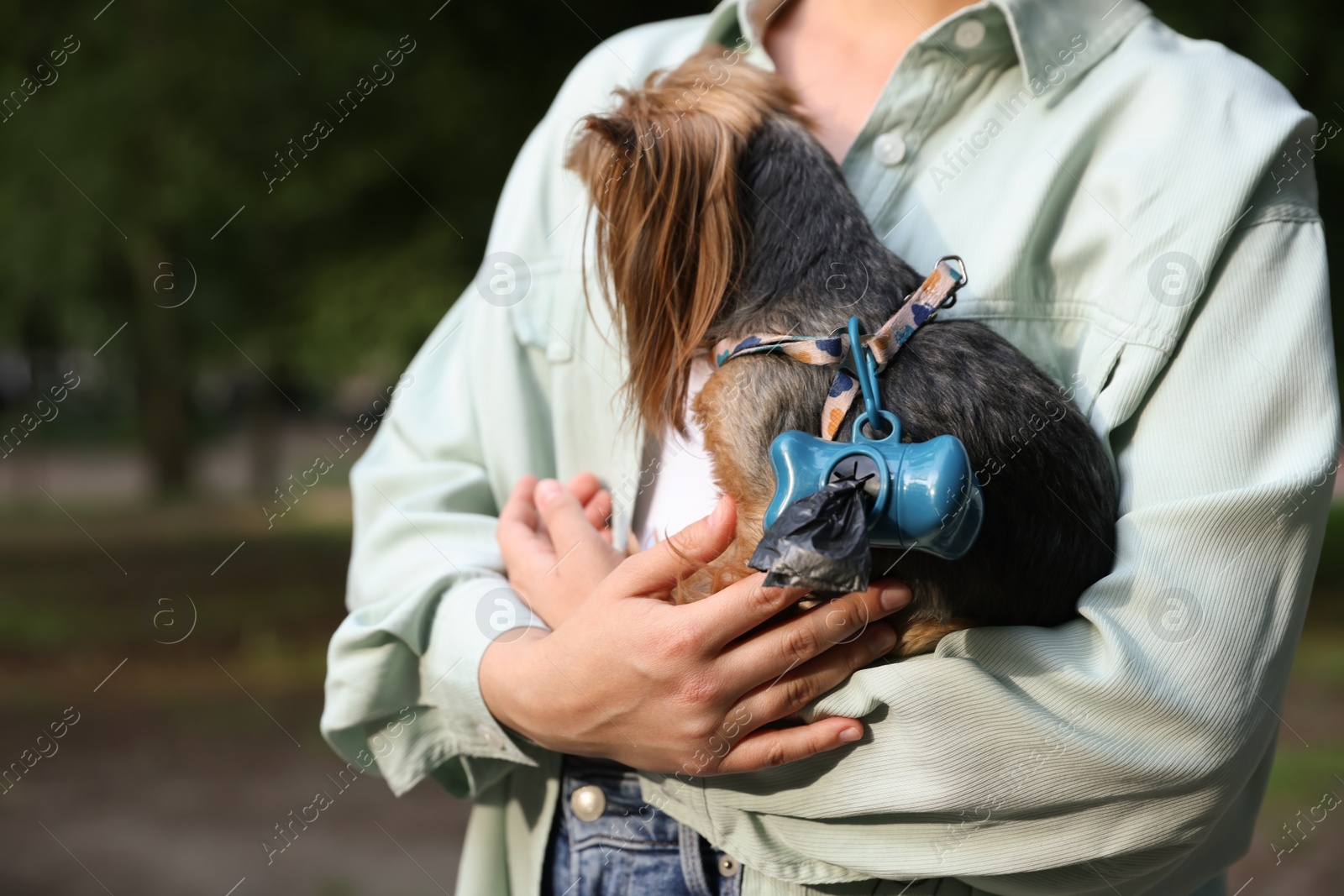 Photo of Woman holding her cute dog with waste bags in park, closeup