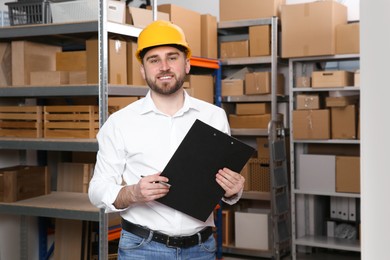 Young man with clipboard near rack of cardboard boxes at warehouse