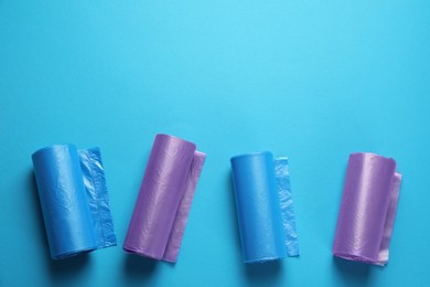 Rolls of different garbage bags on light blue background, flat lay. Space for text