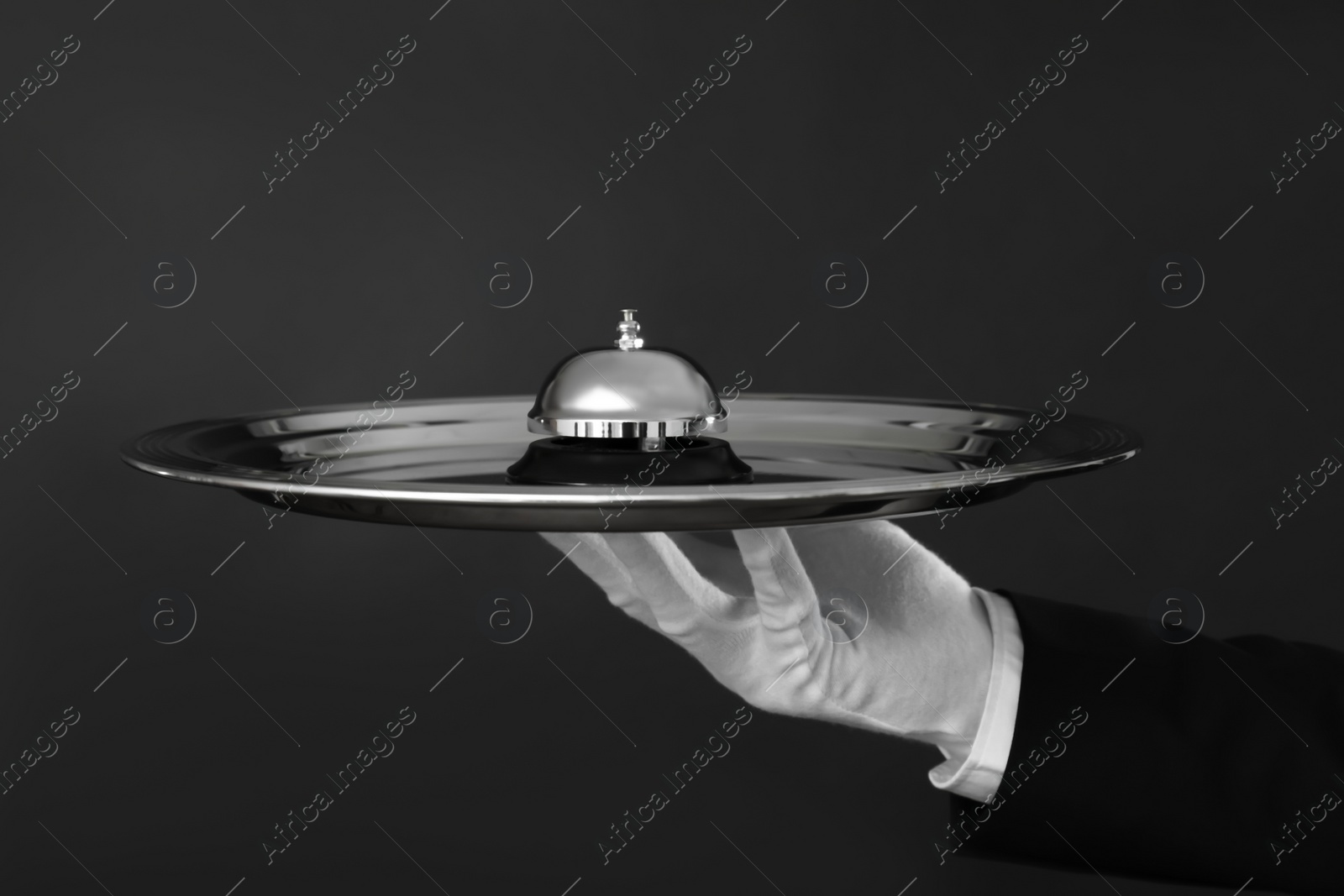 Photo of Butler holding metal tray with service bell on black background, closeup