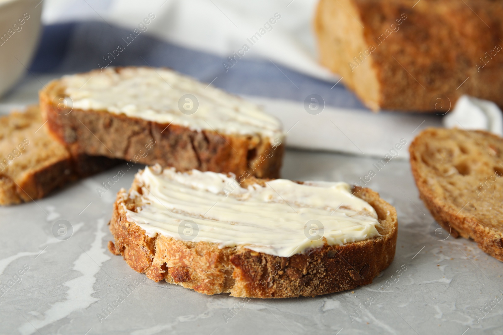 Photo of Slices of tasty bread with butter on grey marble table