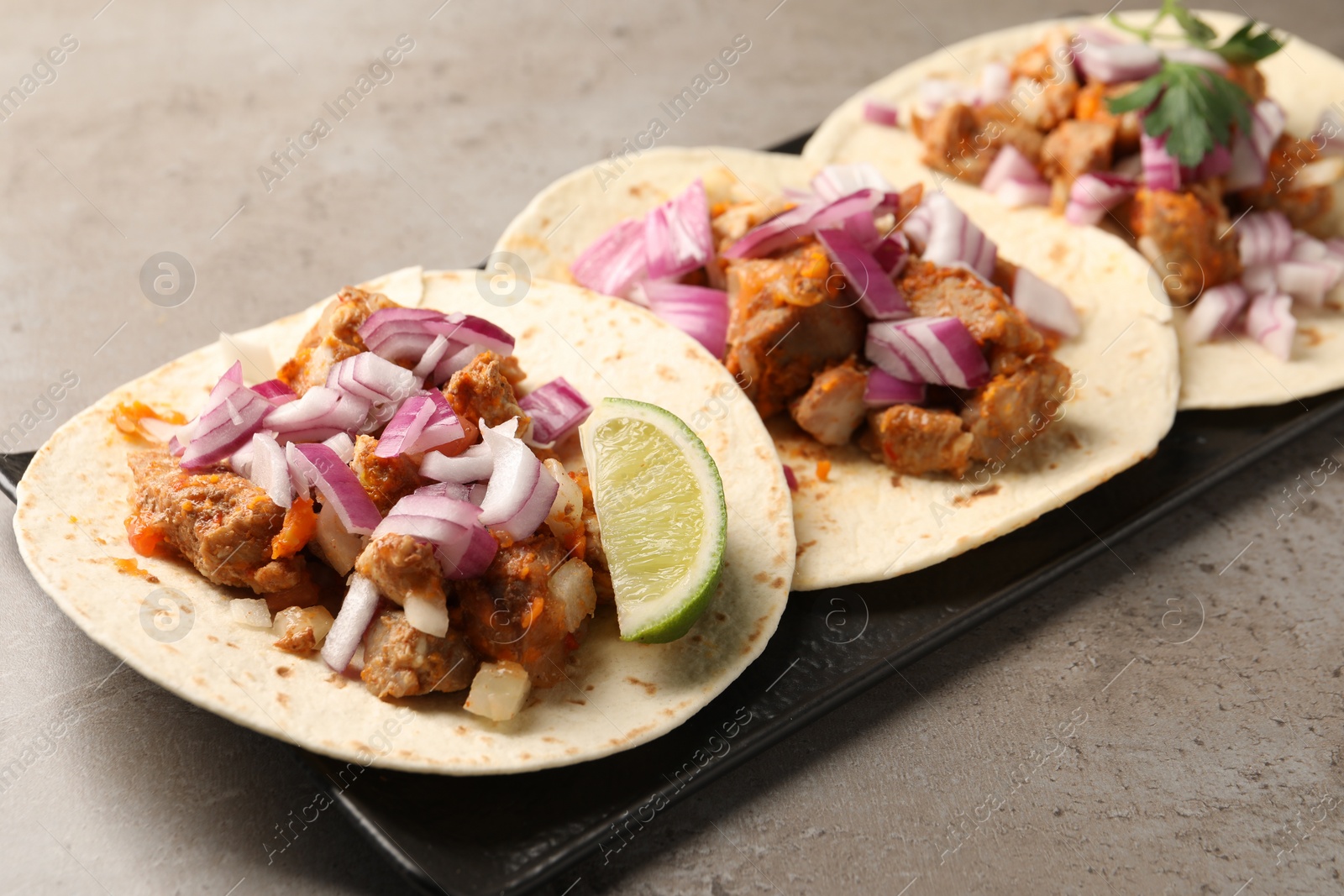 Photo of Delicious tacos with vegetables, meat and lime on grey textured table, closeup