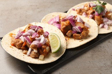 Delicious tacos with vegetables, meat and lime on grey textured table, closeup