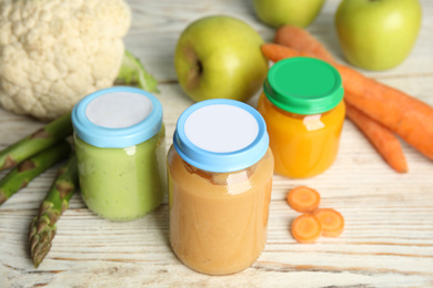 Jars with baby food and fresh ingredients on white wooden table