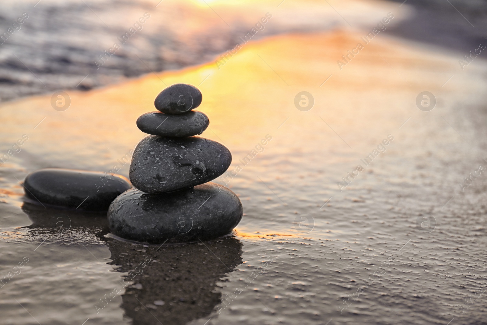 Photo of Dark stones on sand near sea at sunset, space for text. Zen concept