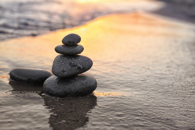 Photo of Dark stones on sand near sea at sunset, space for text. Zen concept