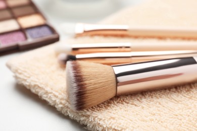 Photo of Clean makeup brushes with towel on white table, closeup