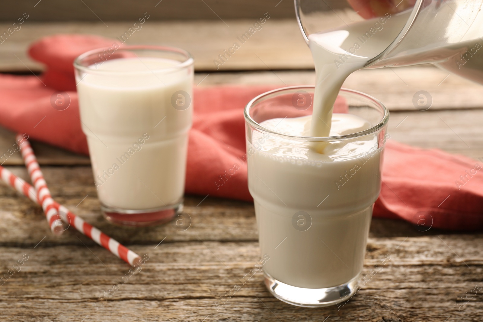 Photo of Pouring tasty milk into glass on wooden table, closeup