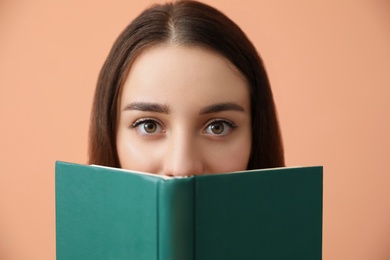 Beautiful young woman reading book on coral background